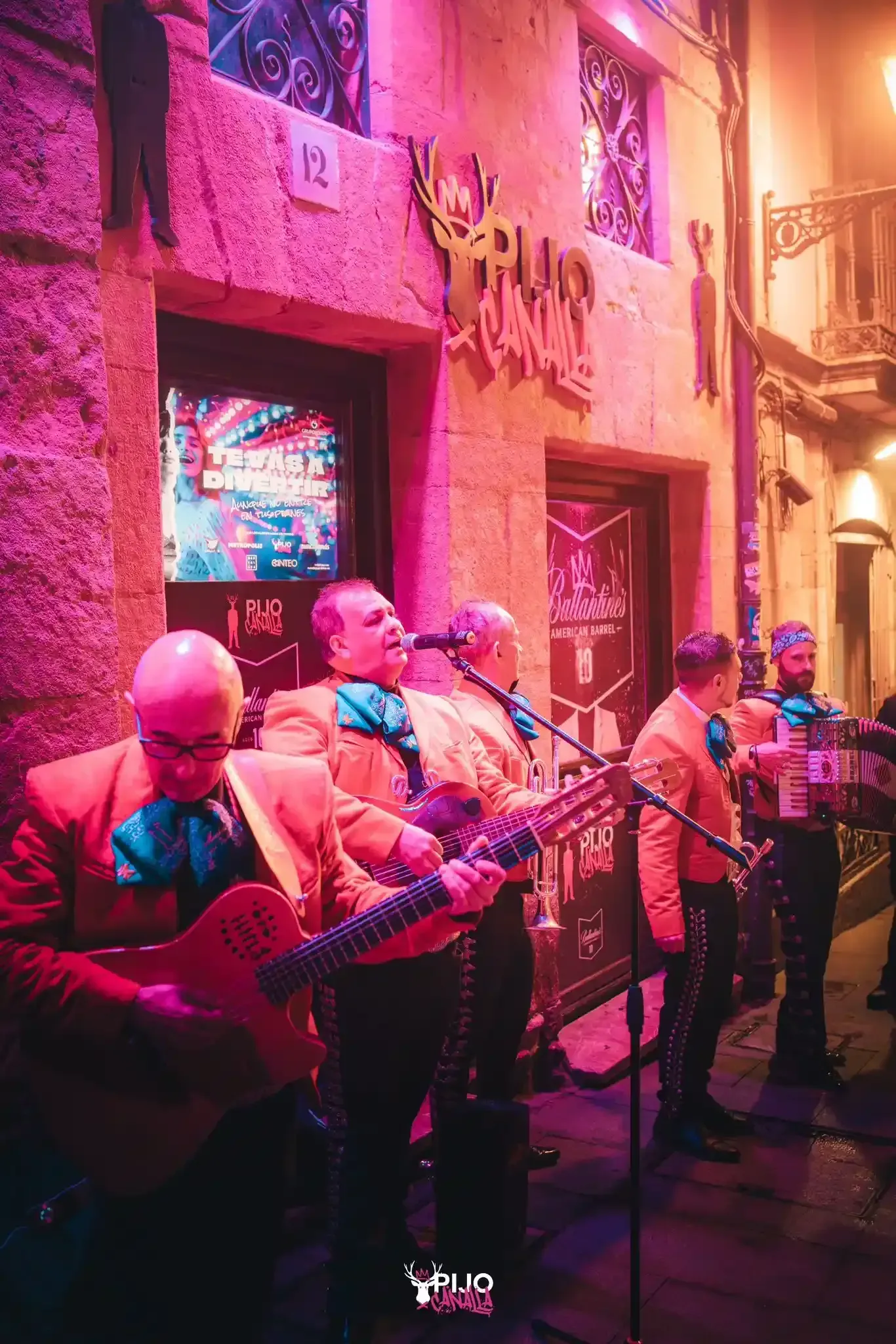 Músicos actuando en directo en un callejón estrecho iluminado con luces de neón rosas y naranjas.