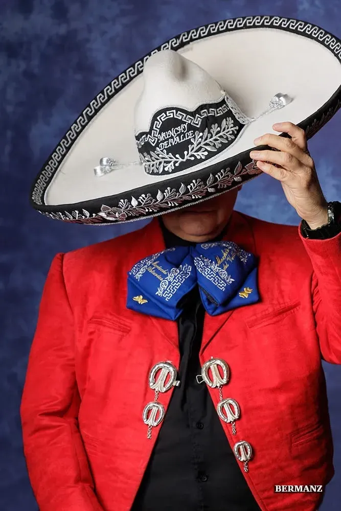 Persona con chaqueta roja y sombrero grande, con la cabeza inclinada, sobre un fondo azul liso.