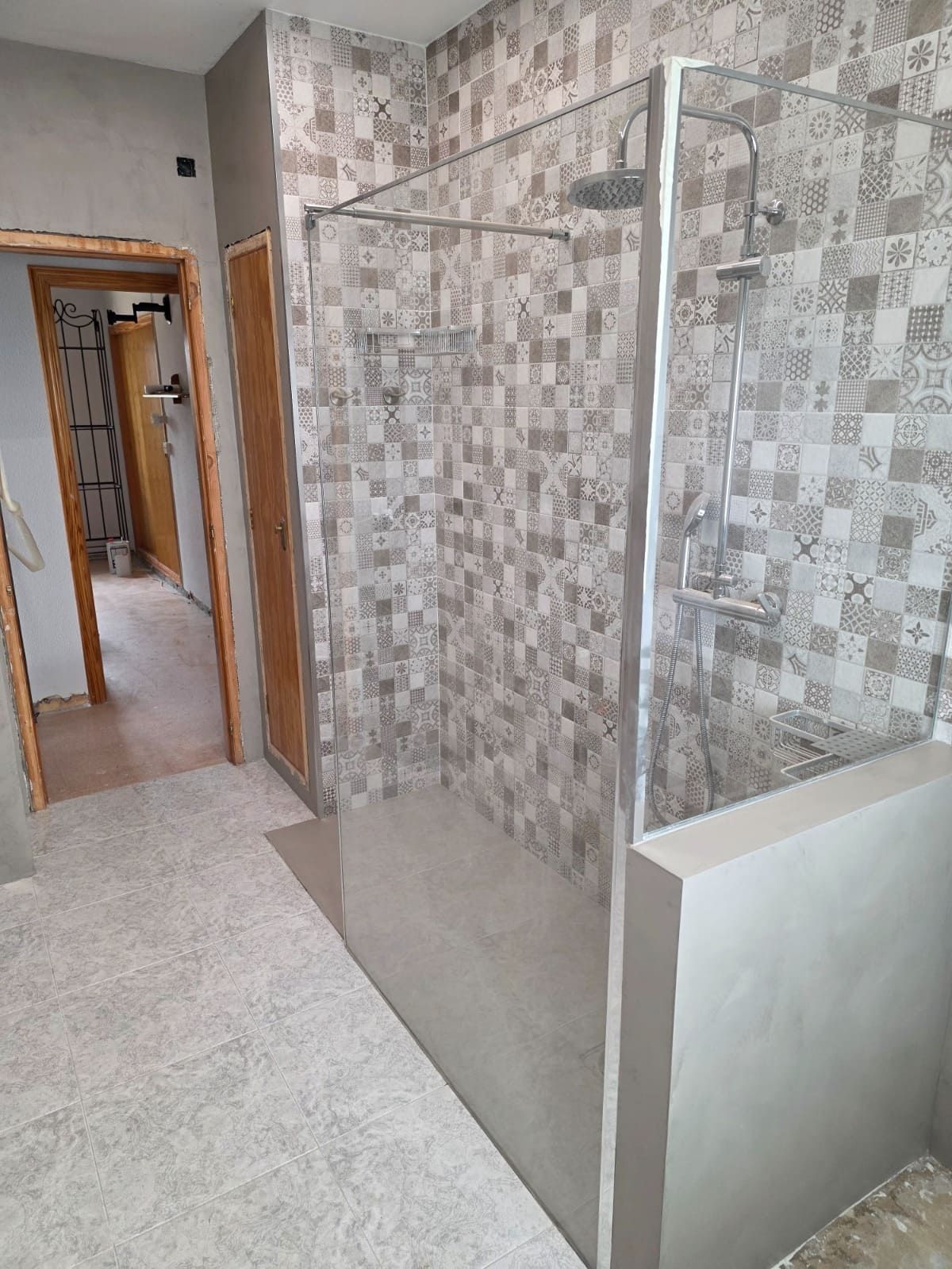 Baño moderno con cabina de ducha de cristal y paredes de azulejos estampados que dan a un pasillo.