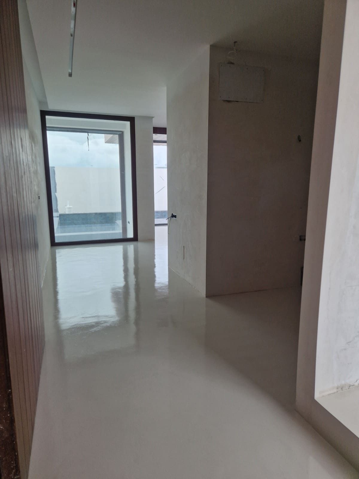 Pasillo moderno y vacío con suelo blanco brillante y una gran puerta corredera de cristal al final.