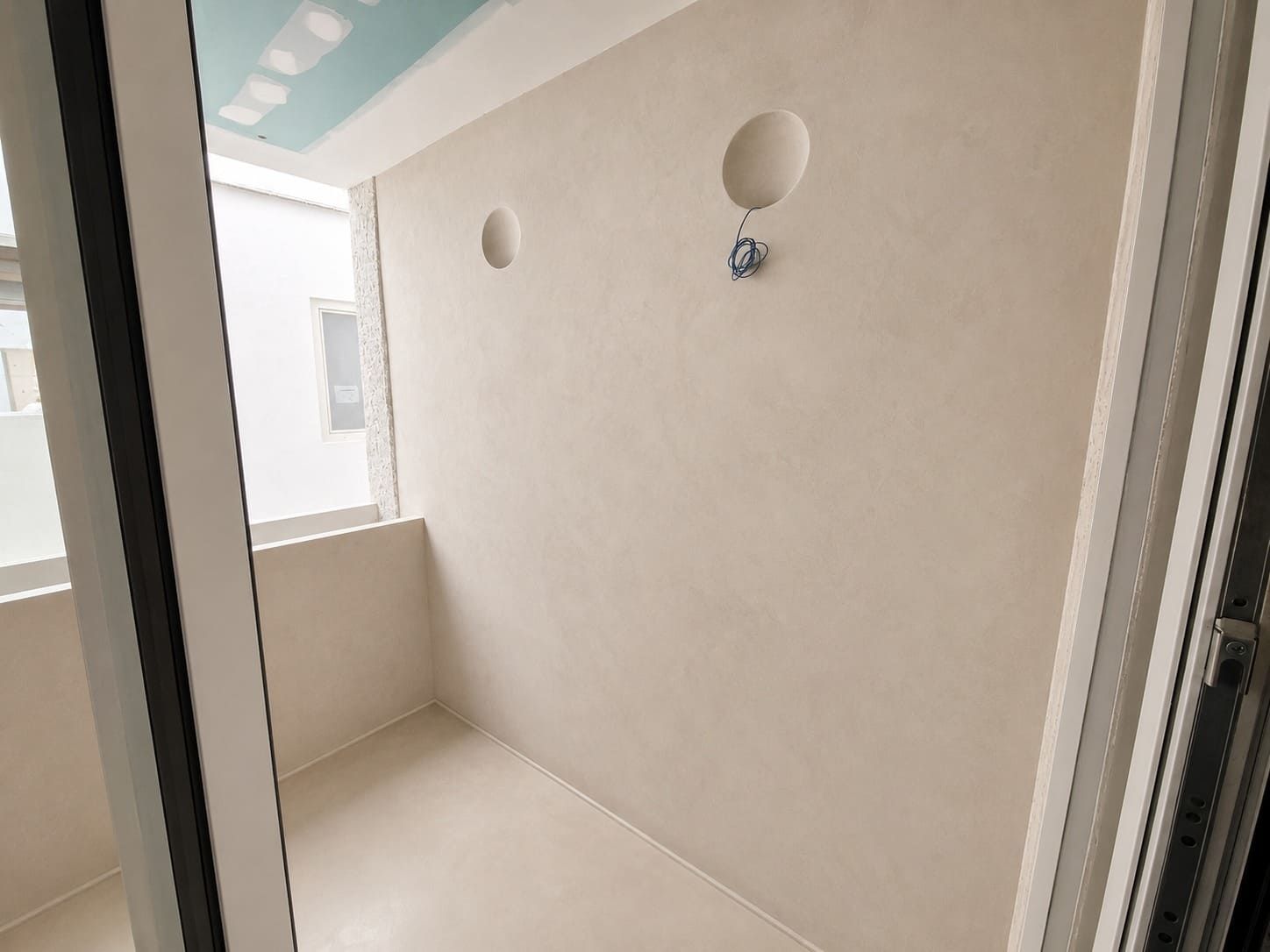 Balcón vacío de color beige con aberturas redondas en la pared y una pequeña lámpara de techo bajo un toldo color verde azulado.