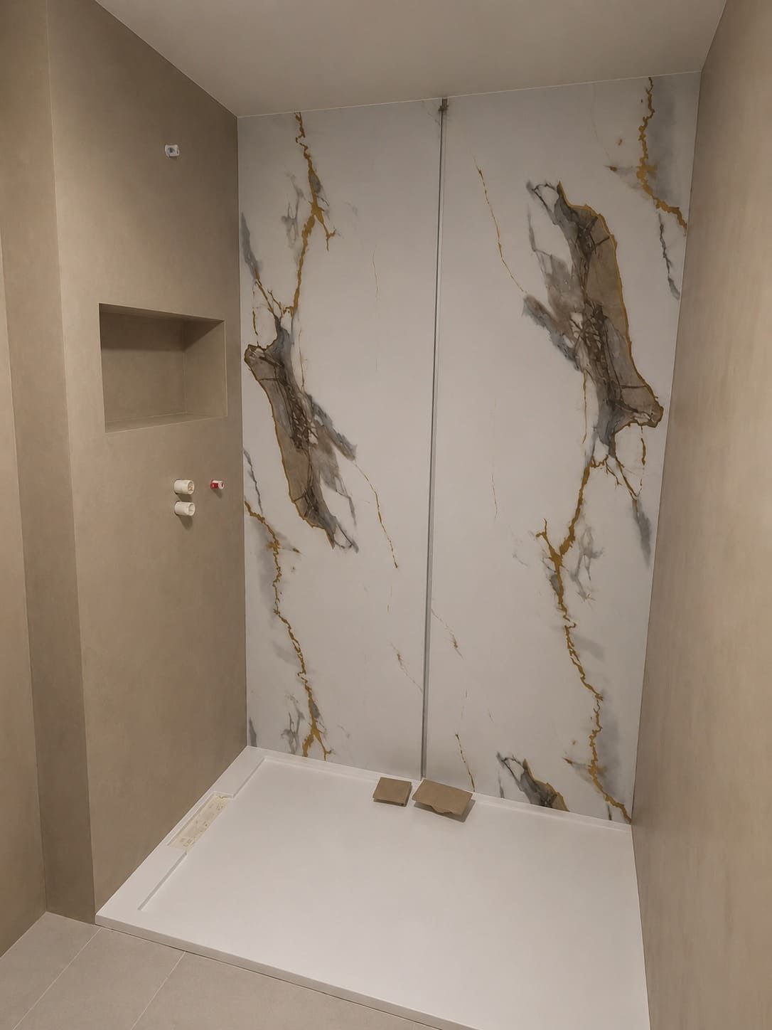 Baño pequeño sin terminar con paredes beige, suelo blanco y azulejos decorativos con estampado de mármol en construcción.