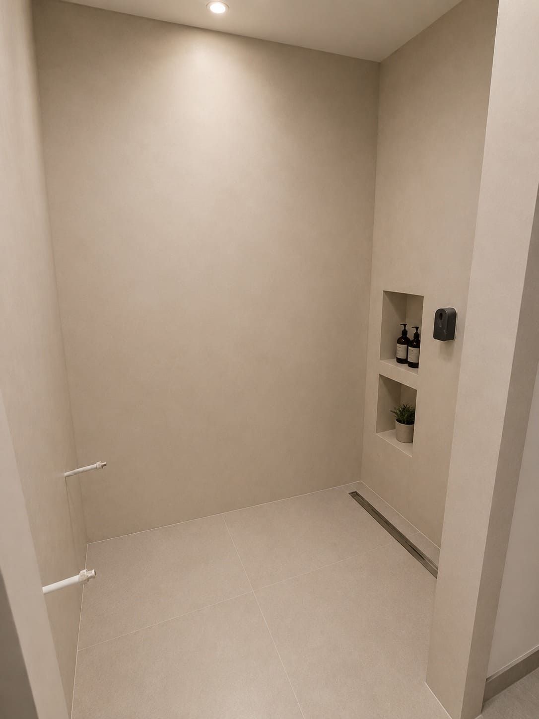 Habitación vacía de color beige con nichos empotrados en la pared y un pequeño escalón que da a un área de baño sin terminar.