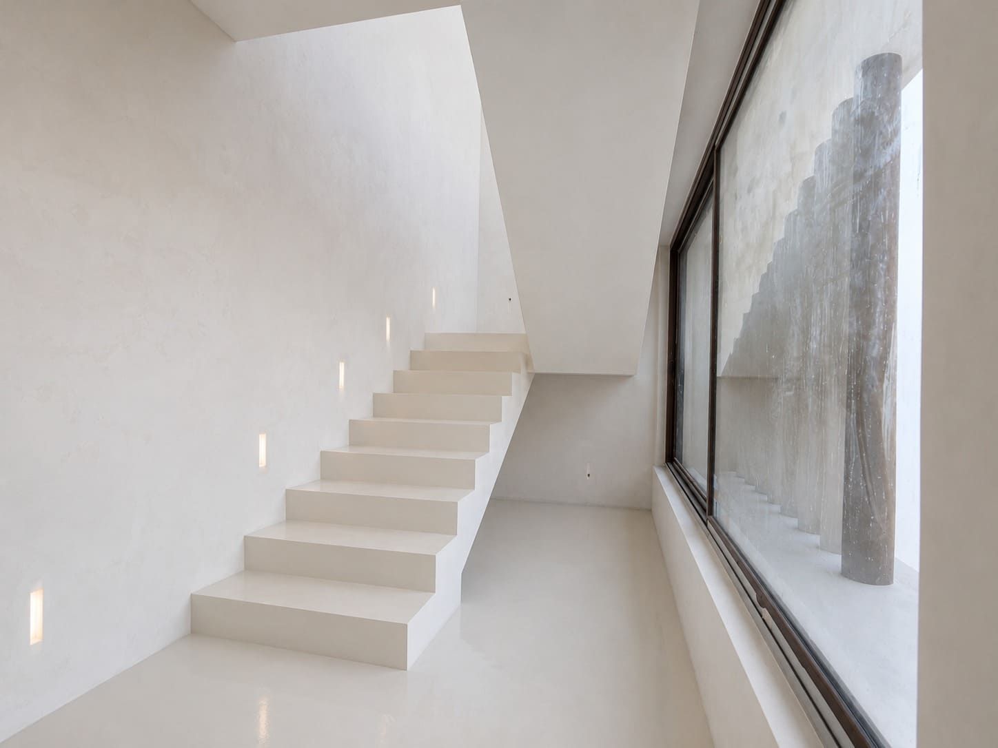 Escalera moderna blanca junto a una gran ventana en un interior minimalista.
