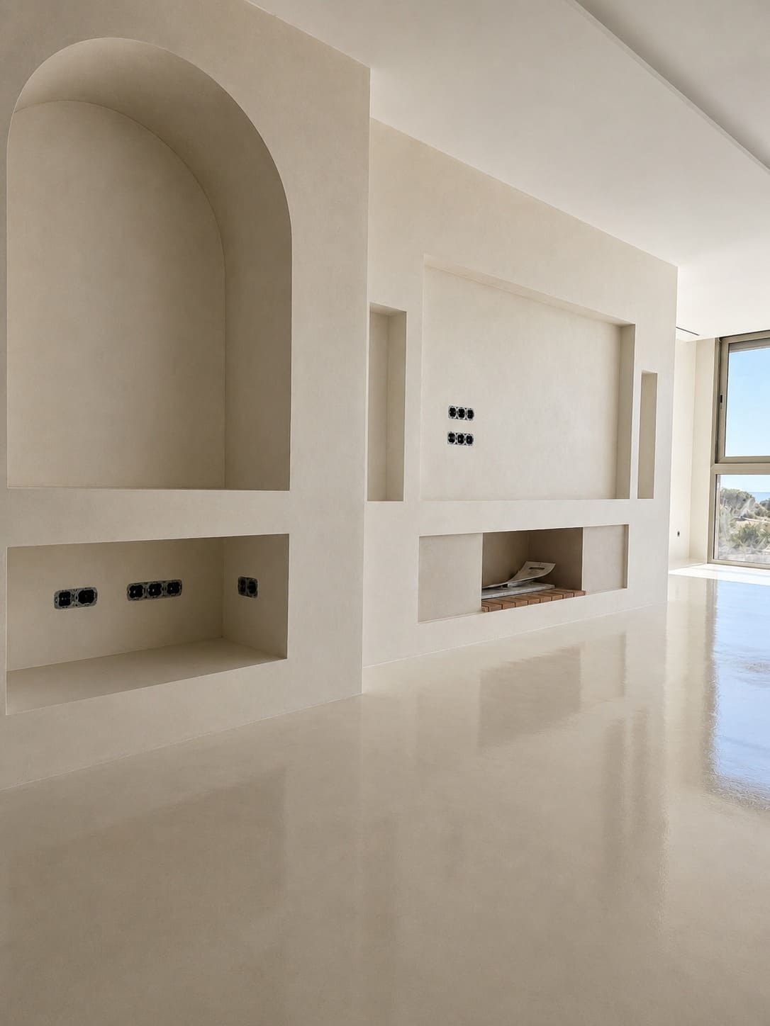 Salón moderno de color beige con nichos empotrados en la pared y suelo de baldosas pulidas, abierto a un exterior luminoso.