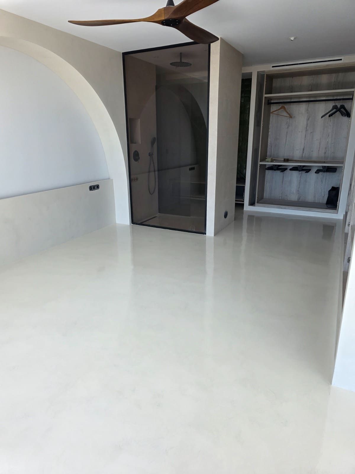 Dormitorio moderno blanco con suelo brillante, detalle de pared arqueada, armario y ventilador de techo.