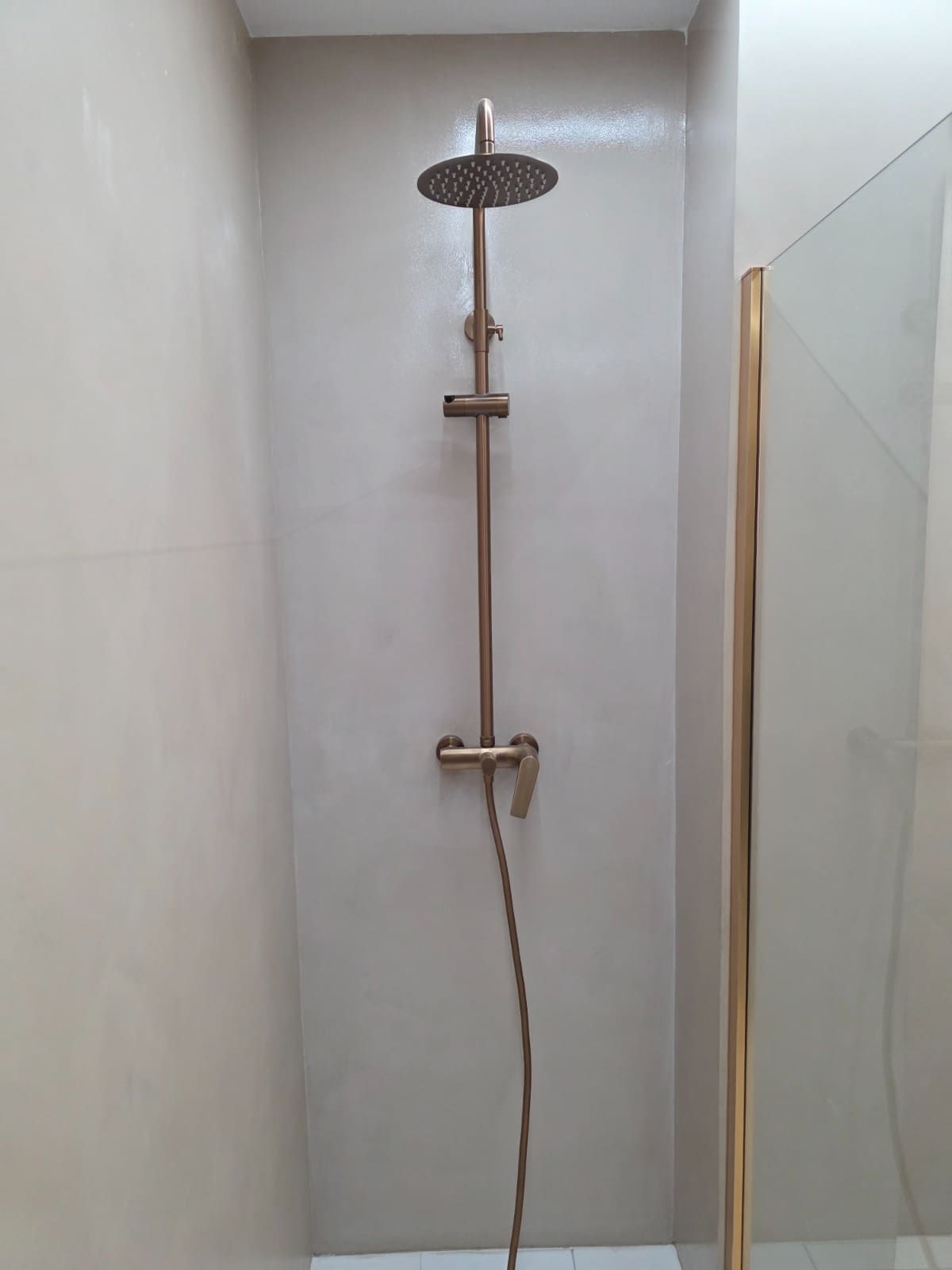 Ducha moderna con cabezal de lluvia montado en la pared y rociador de mano en una cabina alicatada.