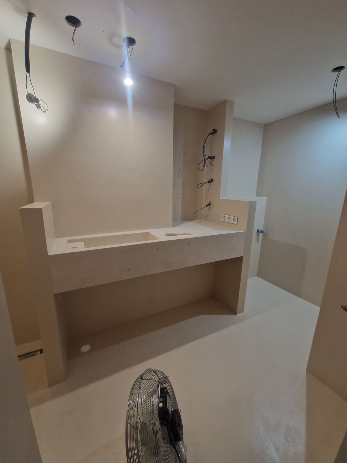 Baño sin terminar con lavabo empotrado, lámparas colgantes y paredes desnudas en construcción.