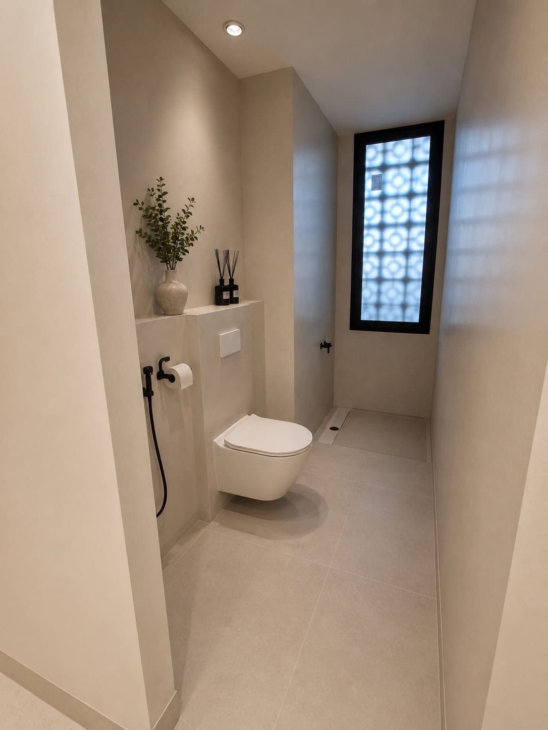 Baño moderno y estrecho con inodoro suspendido, paredes de color beige y ventana esmerilada al final.