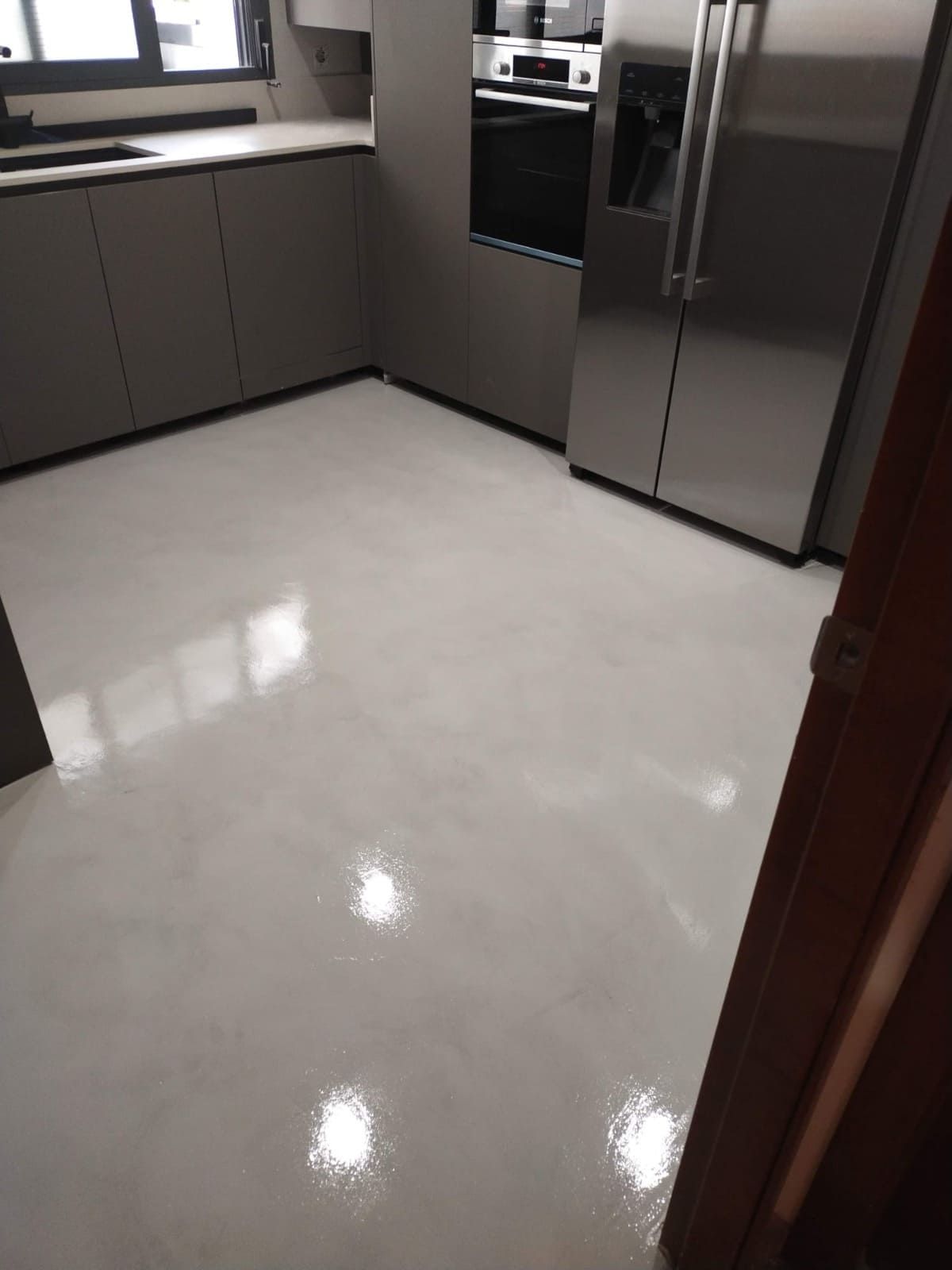 Cocina moderna con suelo blanco brillante, armarios grises y frigorífico de acero inoxidable.