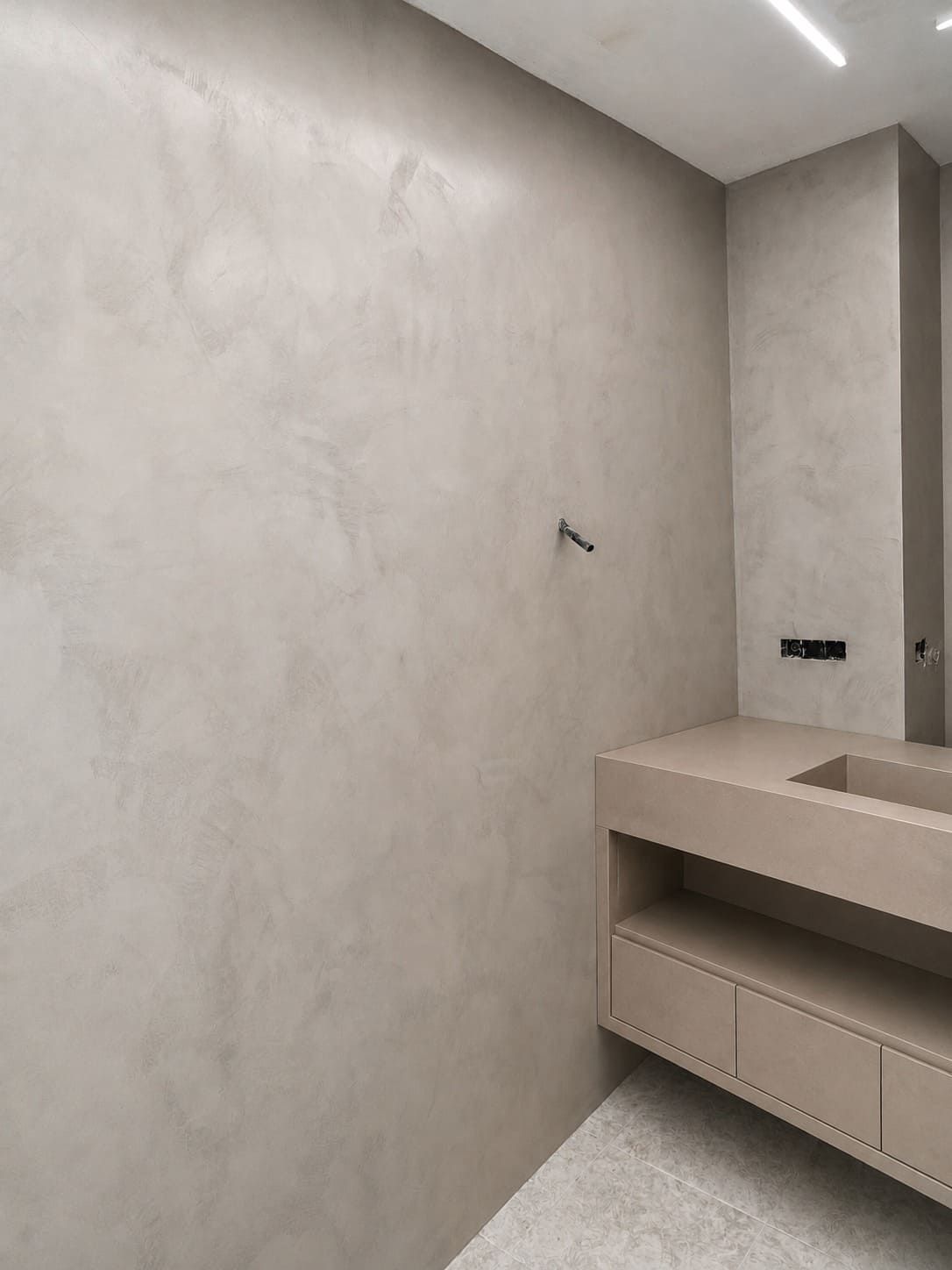 Baño minimalista con paredes de hormigón, lavabo suspendido y luz de pared.