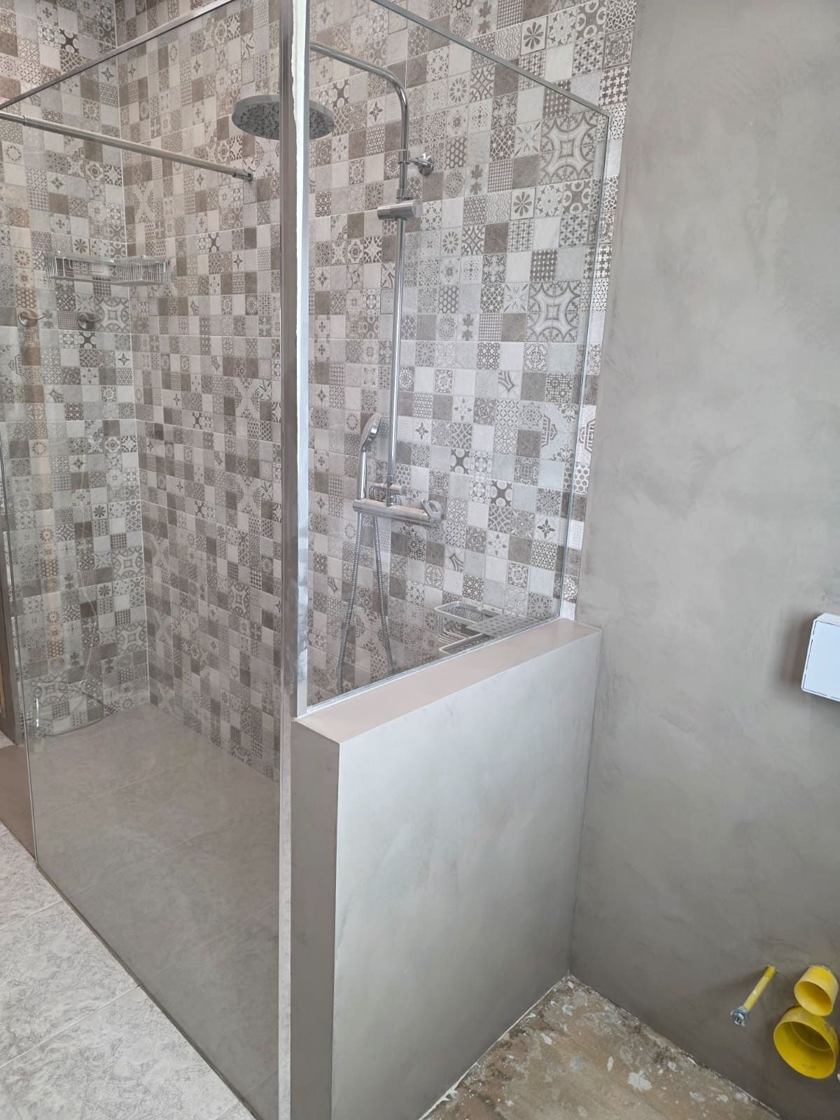En un baño, hay una cabina de ducha alicatada con paneles de vidrio transparente y una mampara esmerilada de media altura.
