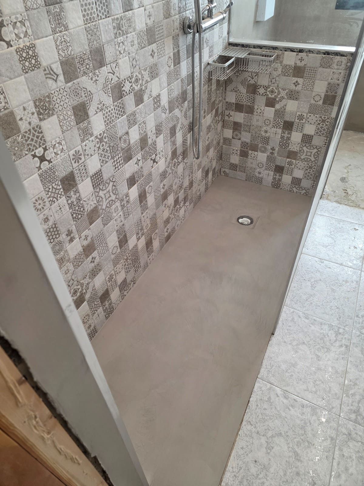 Baño alicatado con suelo de ducha sin azulejos y desagüe, visto desde la puerta.