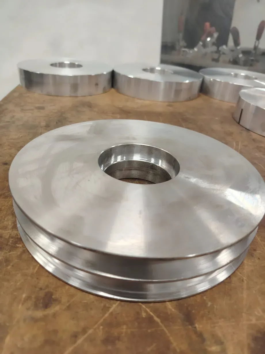 Discos de metal plateado apilados con agujeros centrales sobre un banco de trabajo de madera en un taller.