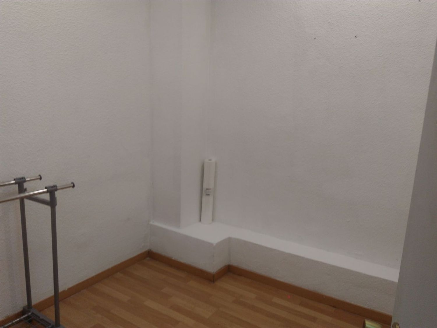 Una pequeña habitación con suelo de madera y paredes blancas.