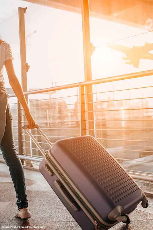 Frau zieht einen Rollkoffer in einem Flughafen. Sonnenuntergang hinter der Flugzeugsilhouette.