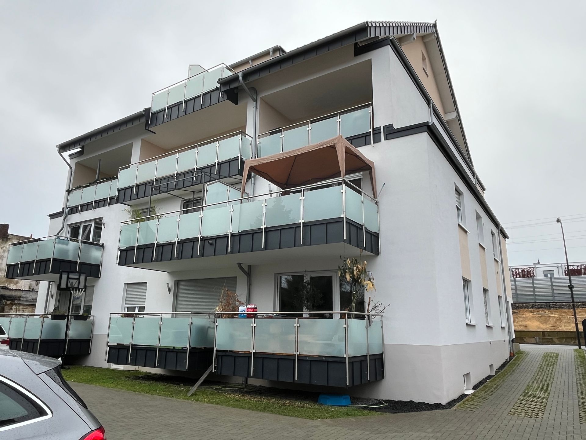 Ein weißes Gebäude mit Balkonen und einem davor geparkten Auto