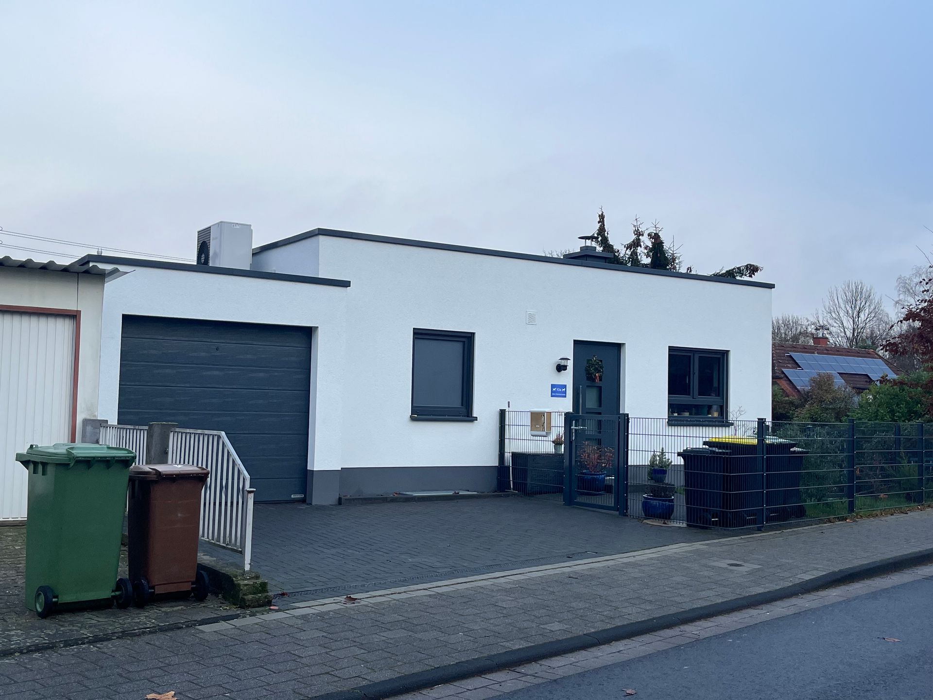 Ein weißes Haus mit einer Garage und Mülltonnen davor