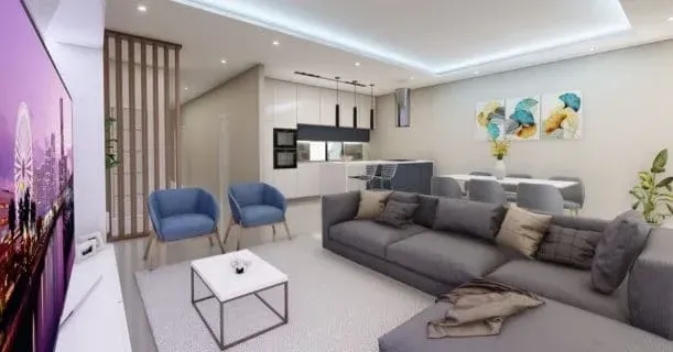 Sala de estar moderna com sofá secional cinza, poltronas azuis e cozinha americana com área de jantar. 