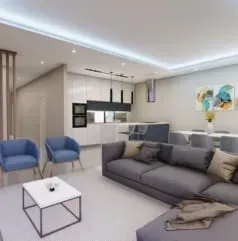 Sala de estar moderna com sofá secional cinza, poltronas azuis e cozinha aberta com armários brancos.