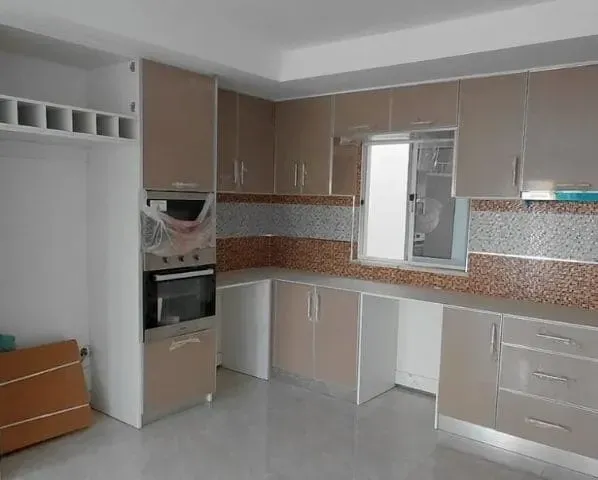Uma cozinha moderna com armários brancos e bege, um forno embutido e uma janela com um backsplash colorido.