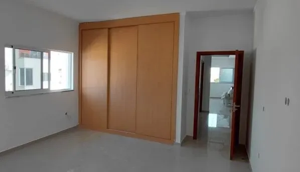 Um quarto com um armário de cor clara, uma janela e uma porta que leva a outro quarto com uma cama.