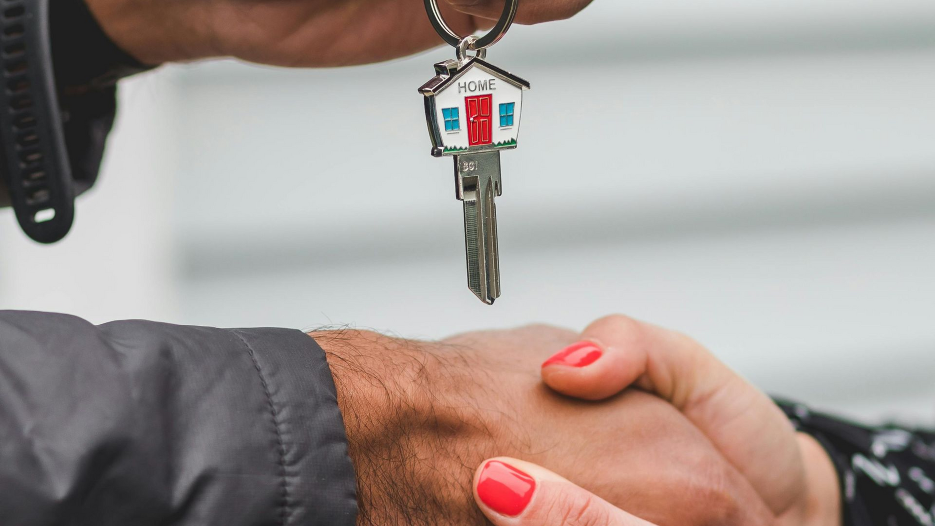 Duas pessoas apertando as mãos, uma delas segurando uma casa em miniatura; provavelmente uma transação imobiliária.