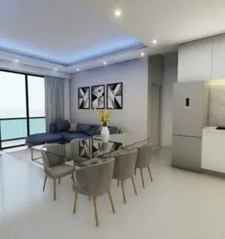 Modern living space with dining area, a gray sofa, and ocean view windows. Neutral tones with touches of blue and yellow.