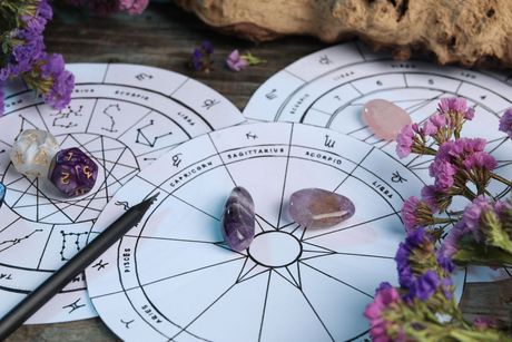 Un lápiz está sobre una carta del zodíaco al lado de flores moradas.