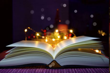 Un primer plano de un libro abierto con luces navideñas en el fondo.
