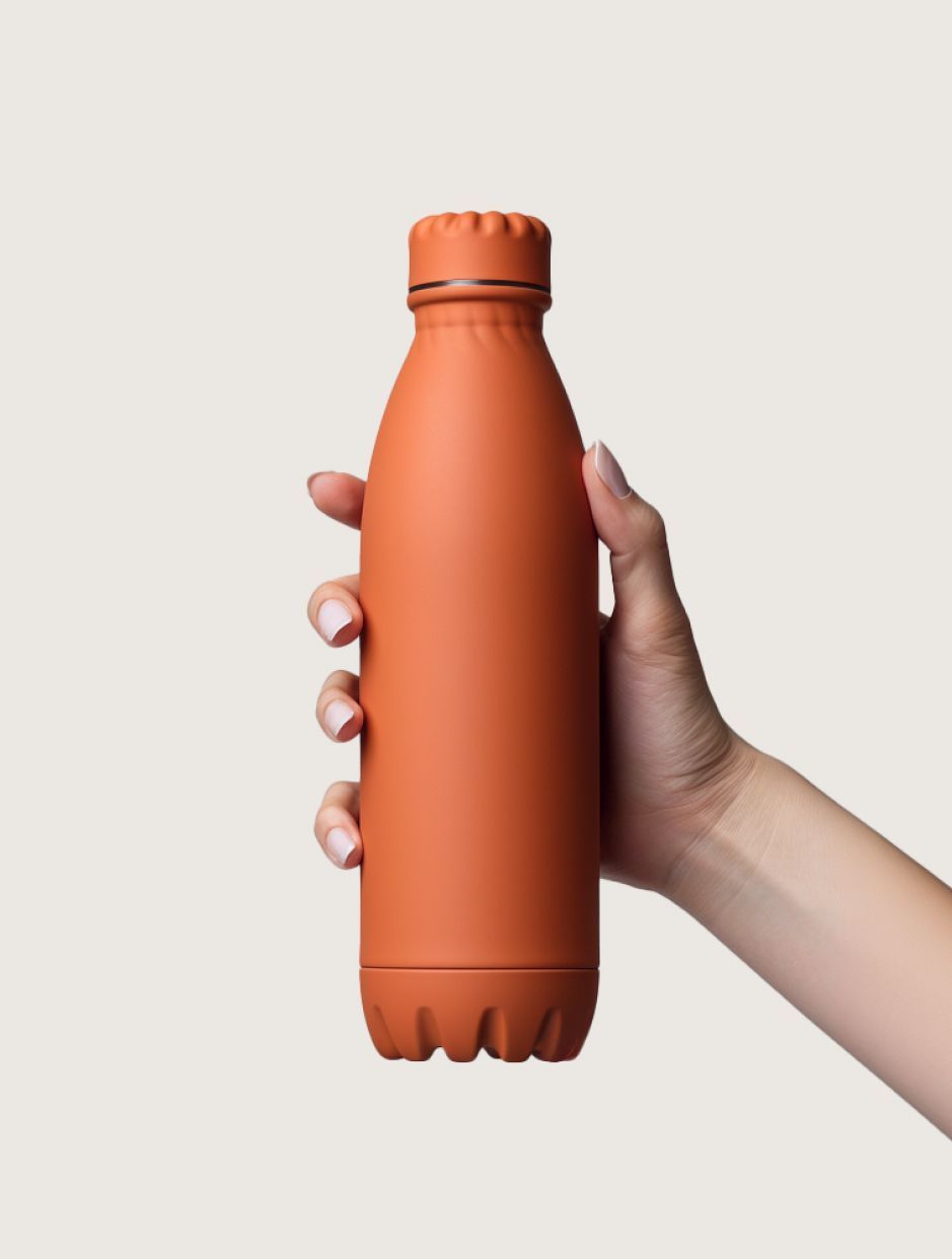 A hand holds a matte, terracotta-colored reusable water bottle against a plain, light background.