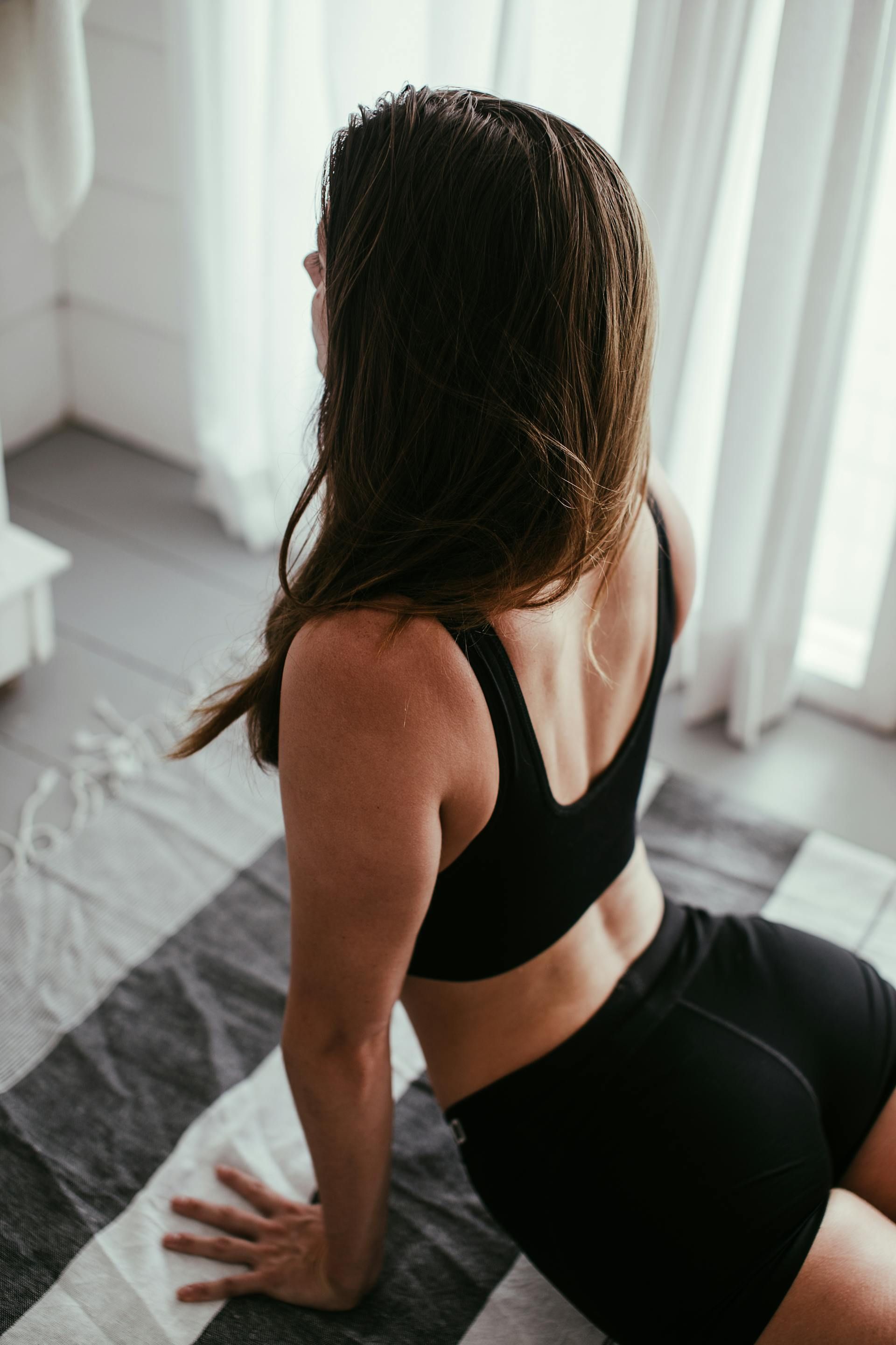 A person with wavy hair wearing a coral sports bra poses against a neutral background, holding a textured pink foam roller.