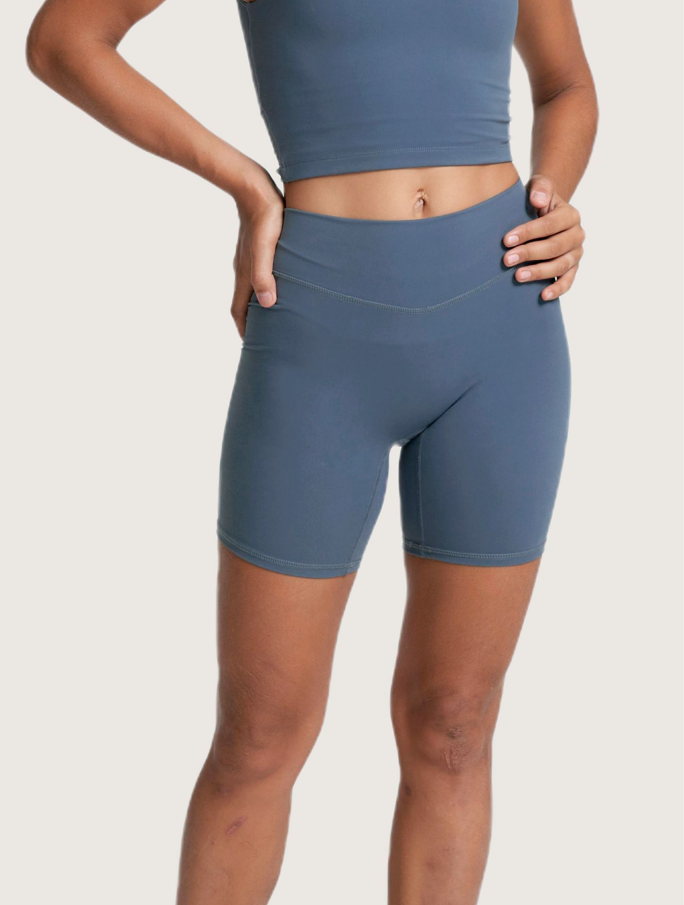 A person wears a blue, high-waisted, seamless workout tank top and matching mid-thigh length athletic shorts.