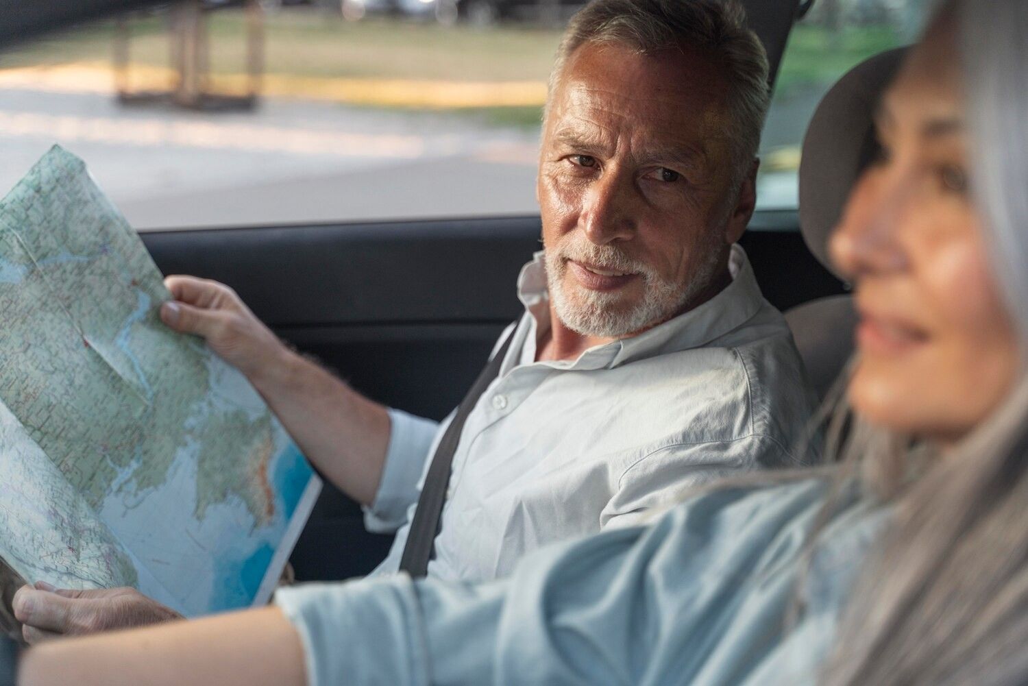 Una persona dentro de un coche sostiene un mapa de papel mientras mira a otra persona.