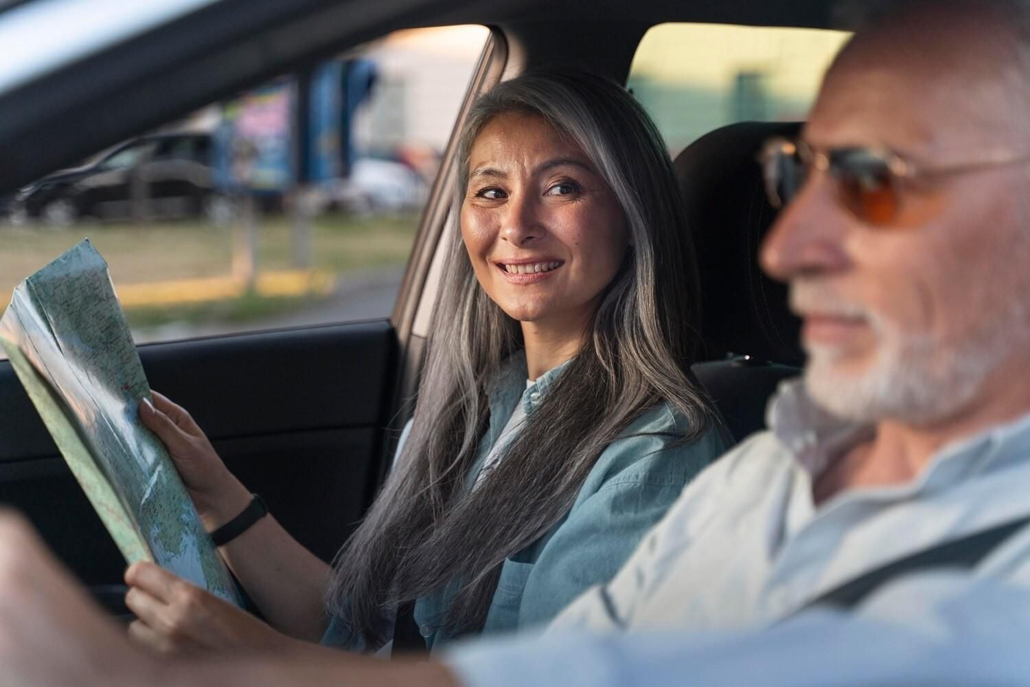 Una persona sonriente dentro de un coche sostiene un mapa