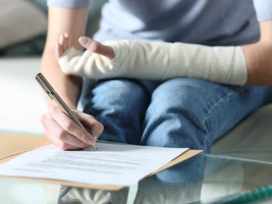 Una persona con un yeso en el brazo está escribiendo en un trozo de papel.