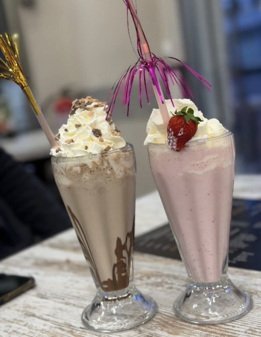 Dos batidos en copas de cristal, uno de chocolate y otro de fresa, coronados con nata montada y una cereza.