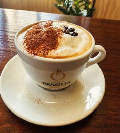 Un capuchino con cacao en polvo y granos de café sobre un platillo en una mesa de madera.