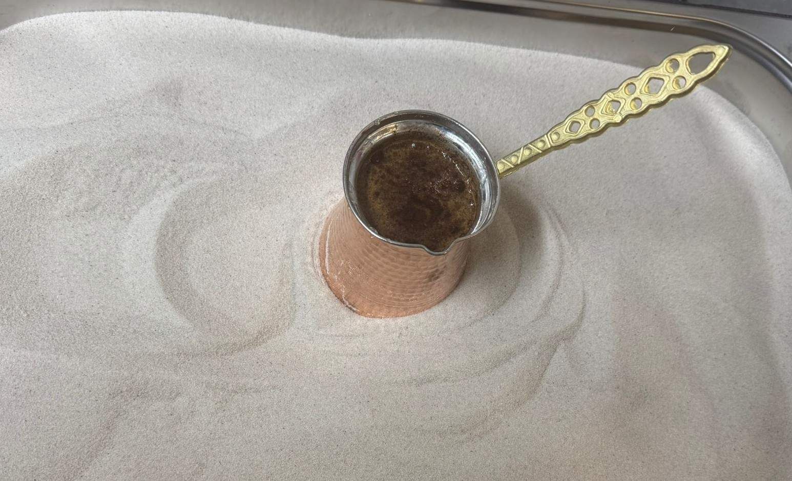 Una pequeña taza de metal sobre un paño blanco, con una cuchara de mango dorado a su lado.
