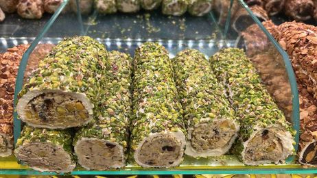 Bandeja de pasteles enrollados cubiertos de pistacho sobre un mostrador de cristal, con los extremos cortados.