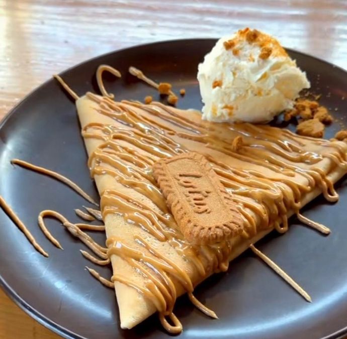 Crepe bañada en caramelo sobre un plato oscuro, cubierta con crema batida y una galleta.