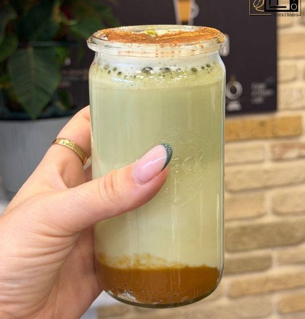 Una mano sostiene una bebida helada espumosa en capas dentro de un frasco de vidrio transparente.