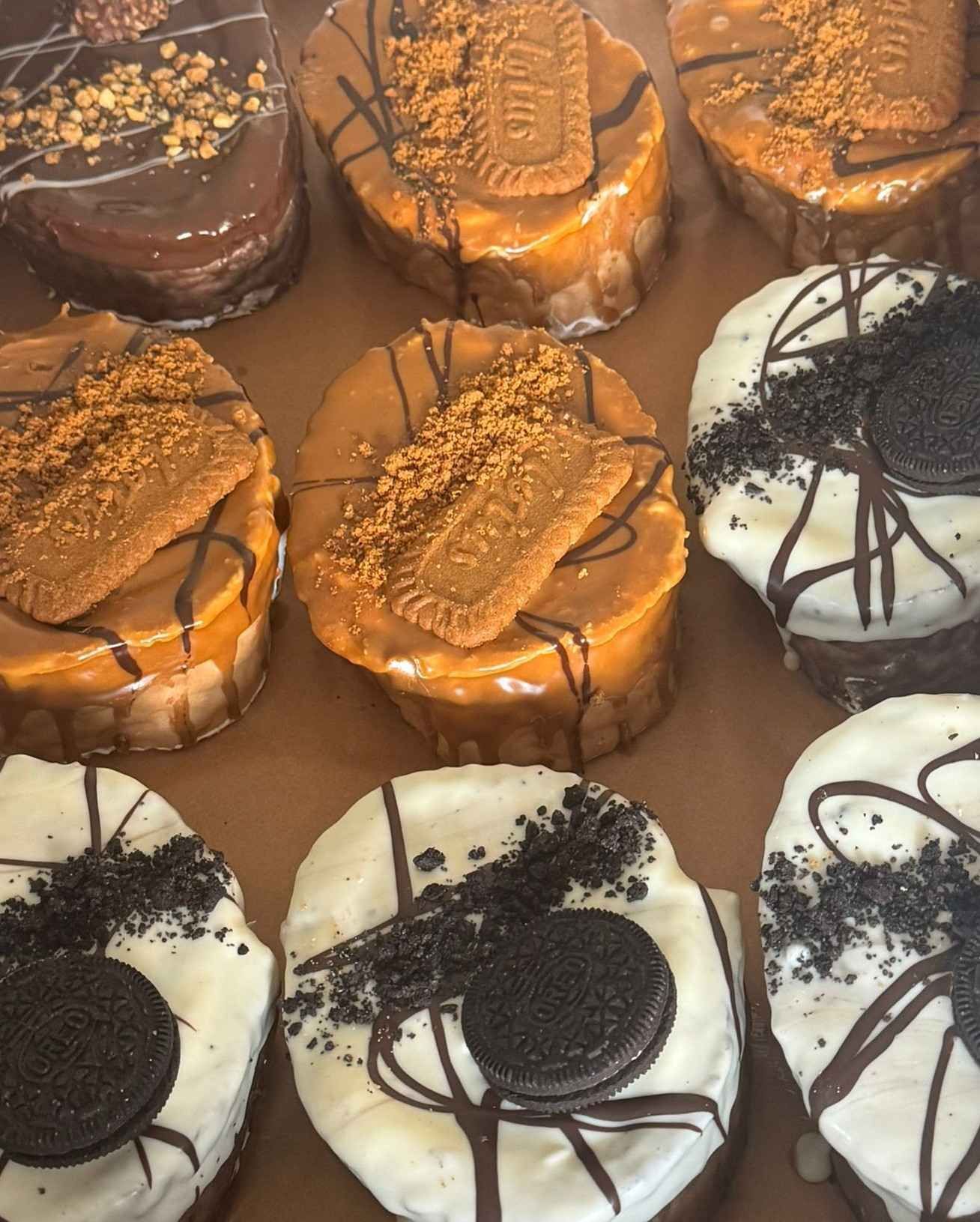 Surtido de donuts decorados en una caja de pastelería, cubiertos con caramelo, sirope de chocolate y galletas trituradas.