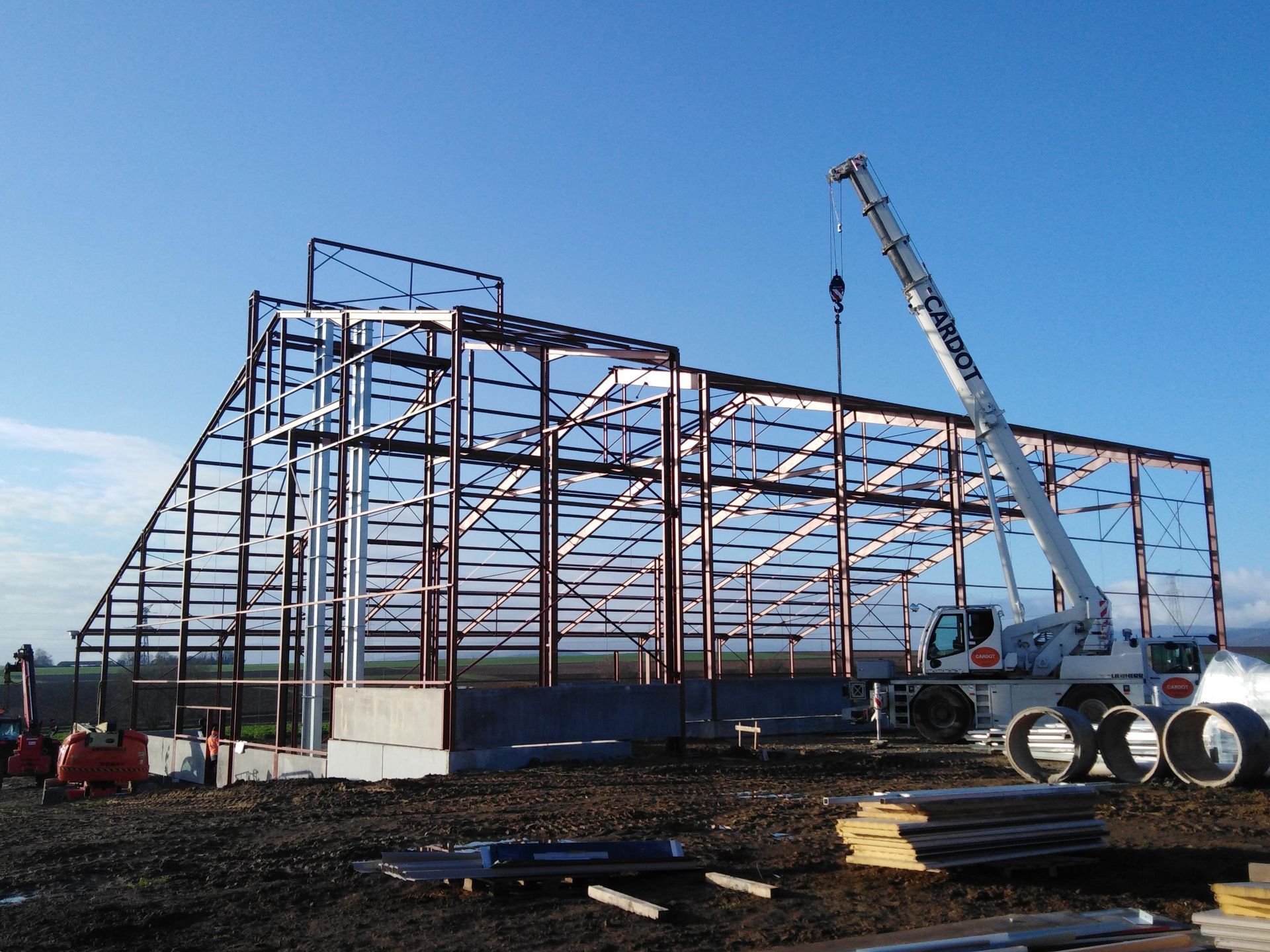 Bâtiment à ossature métallique en construction, avec une grue sur un chantier boueux