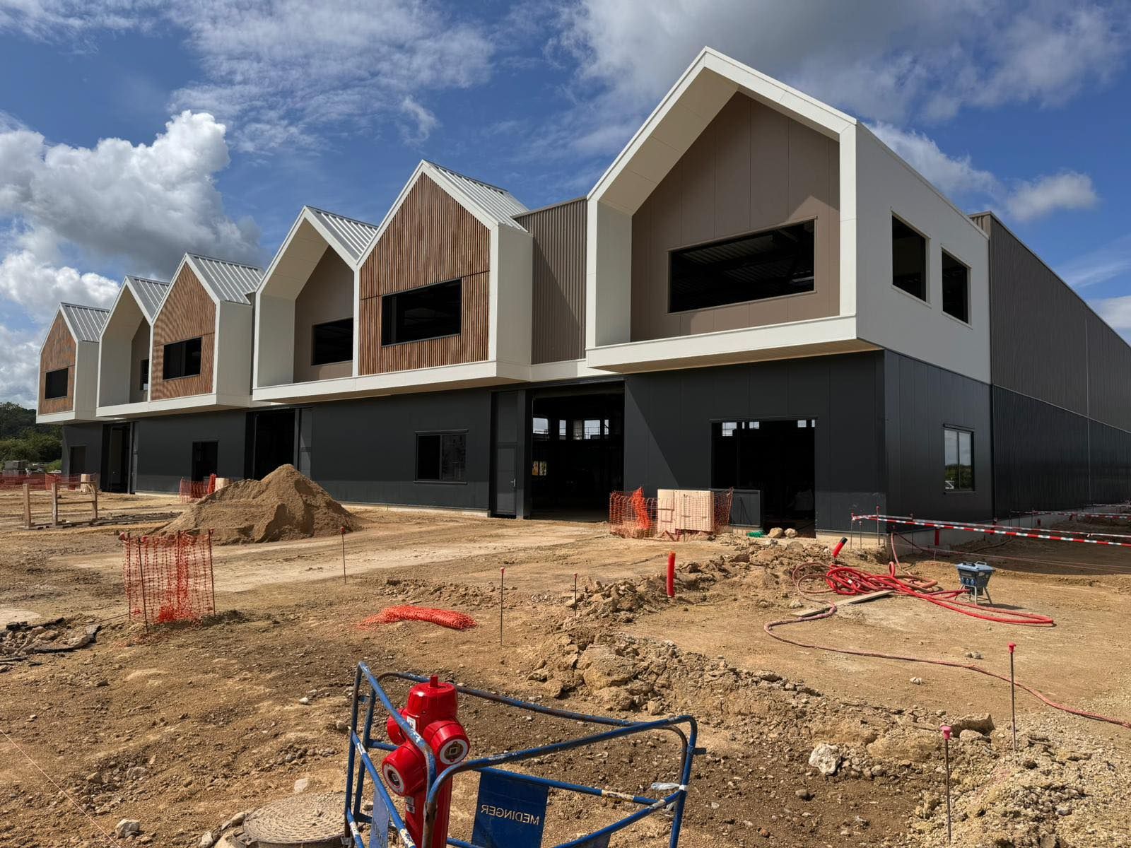 Rangée de maisons de ville modernes en construction, avec leur ossature apparente, sur un terrain en terre, sous un ciel nuageux