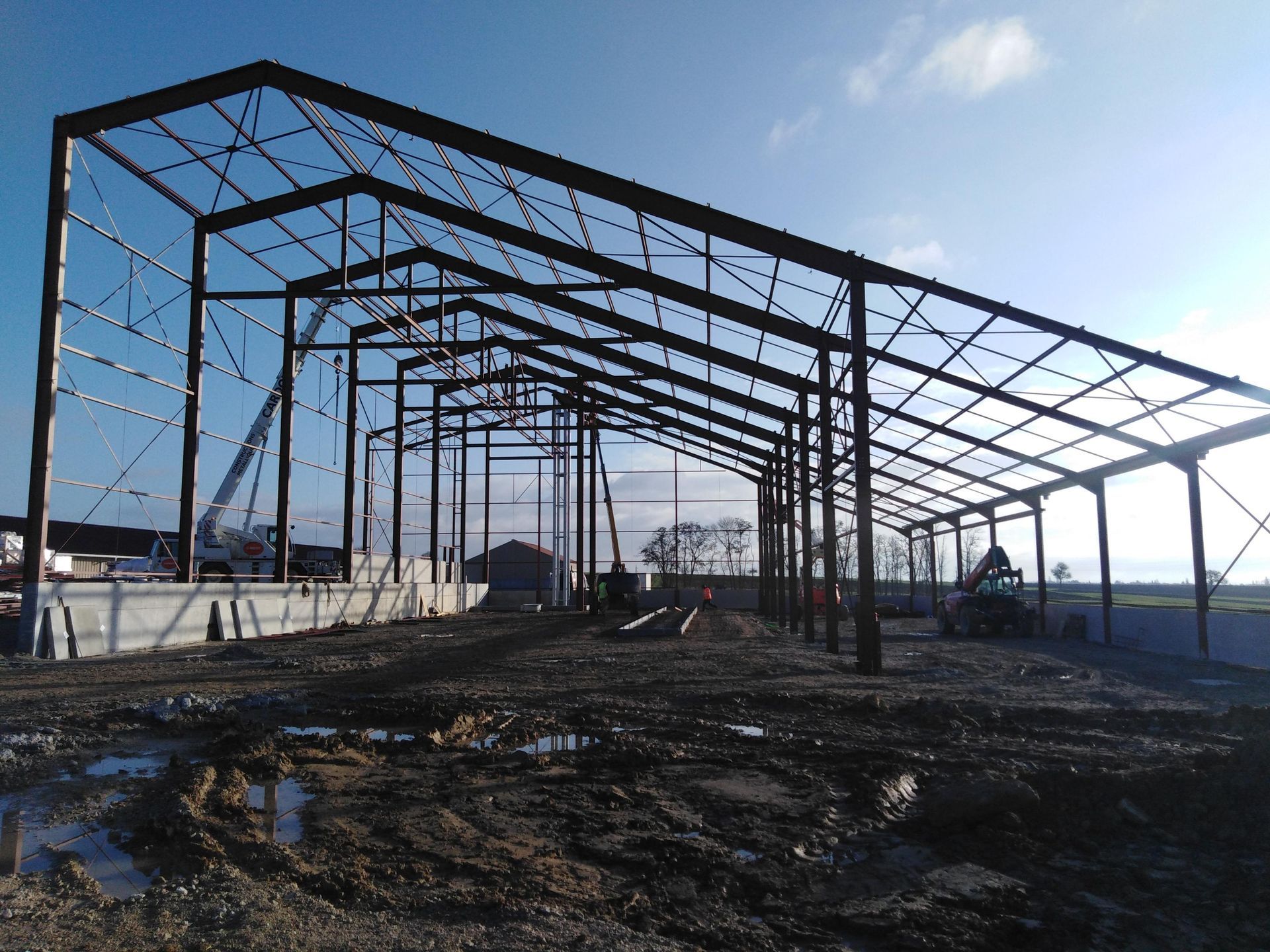 Structure à ossature métallique partiellement construite sur un chantier boueux, sous un ciel bleu