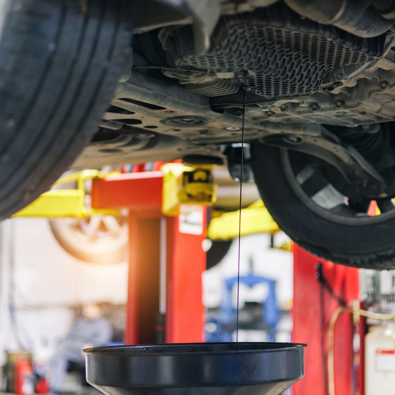 Une voiture surélevée sur un pont élévateur, l'huile moteur s'écoulant dans un bac de récupération.