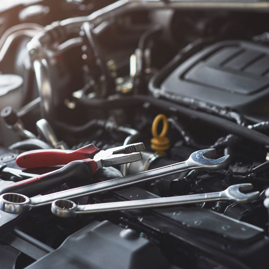 Un jeu de clés métalliques et une pince à poignée rouge posés sur un moteur de voiture.