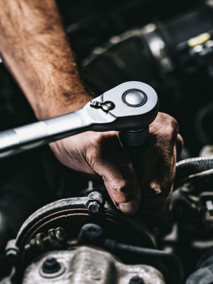 Un mécanicien utilise un outil à cliquet métallique pour travailler sur un moteur de voiture.