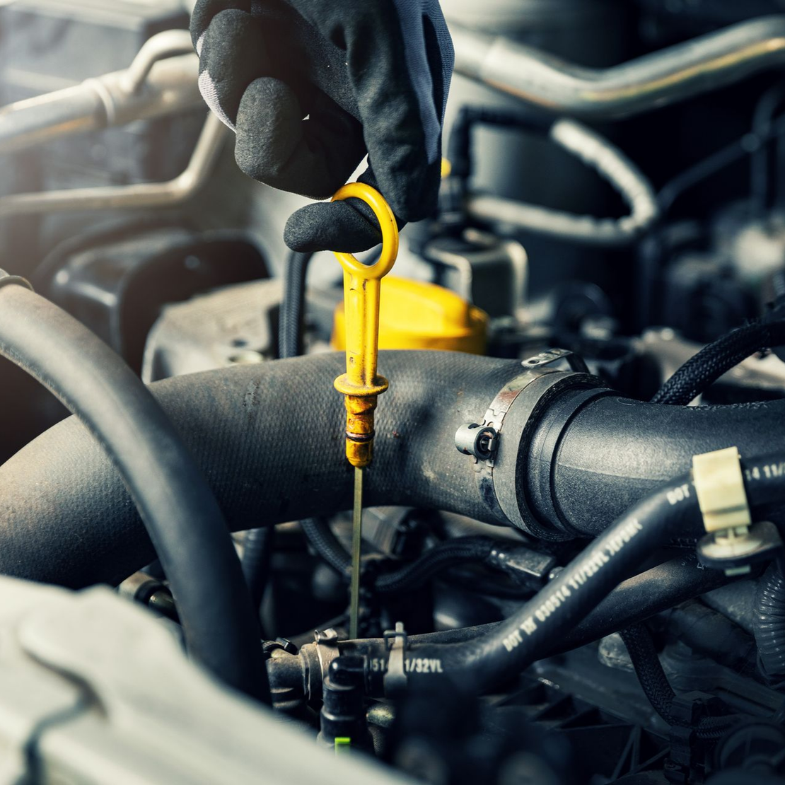 Une main gantée retire une jauge d'huile moteur à poignée jaune du moteur d'une voiture.